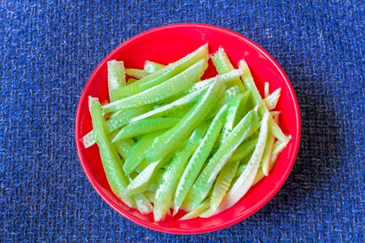 Green strips of cucumbers on scarlet plate on dark blue textile background
