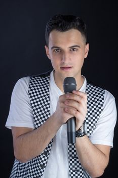 Young black-haired man dressed in black and white performs singing to microphone