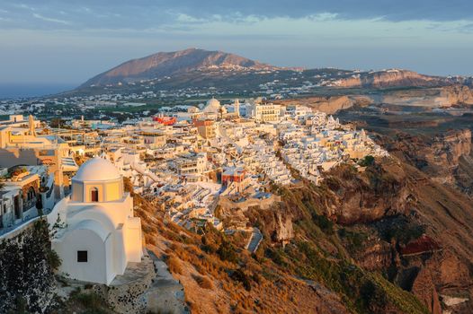 Fira, Santorini island, Greece - April 2016: Illuminated Luxury balcony decks and patios with restaurants of Fira town at Santorini island, in warm rays of sunset. Santorini is one of most famous greek resorts situated in Aegean sea at old volcano's caldera.