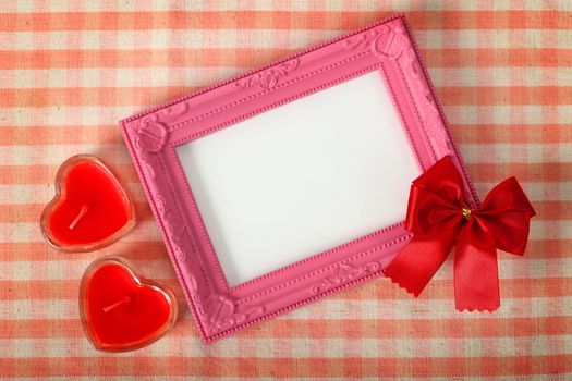 Top view of empty pink photo frame and red ribbon next heart sign from candle over the fabric, clipping path ready to put photographs.