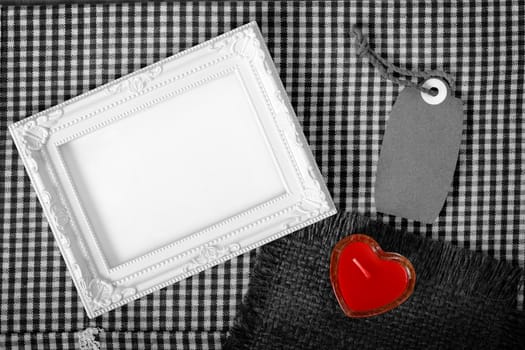 Top view of empty white photo frame next red heart sign from candle and paper tag, clipping path ready to put photographs.