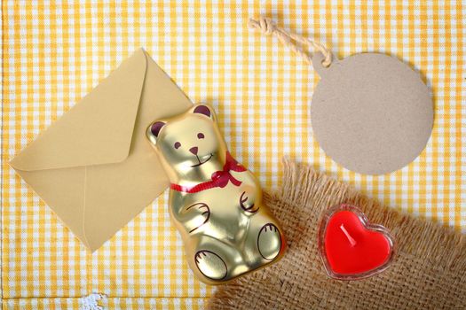 Top view of golden bear and paper tag for text and heart sign from candle in glass over the fabric, concept valentine background.