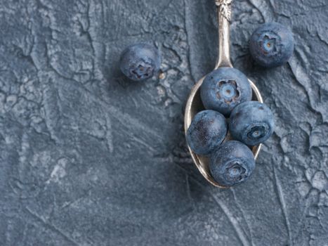 Freshly picked blueberries in spoon closeup. Ripe and juicy fresh blueberry on textured concrete background. Bilberry on dark background with copyspace. Blueberry antioxidant. Top view or flat lay