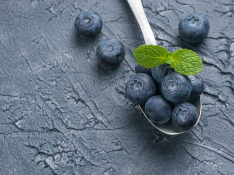 Freshly picked blueberries in spoon closeup. Ripe and juicy fresh blueberry with green mint leaves on textured concrete background. Bilberry on dark background with copyspace. Top view or flat lay