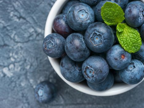 Freshly picked blueberries closeup. Ripe and juicy fresh blueberry with green mint leaves on textured concrete background. Bilberry on gray background with copyspace. Top view or flat lay