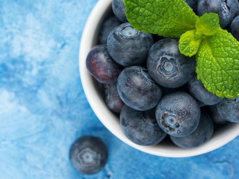 Freshly picked blueberries closeup. Ripe and juicy fresh blueberry with green mint leaves on textured concrete background. Bilberry on blue background with copyspace. Top view or flat lay