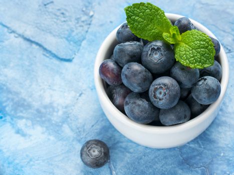 Freshly picked blueberries closeup. Ripe and juicy fresh blueberry with green mint leaves on textured concrete background. Bilberry on blue background with copyspace. Top view or flat lay