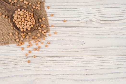 Chickpeas in a wooden spoon and an old white wooden table. Top view.