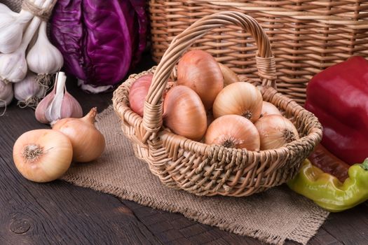 Onions in a wicker basket on old wooden table. Selective focus.