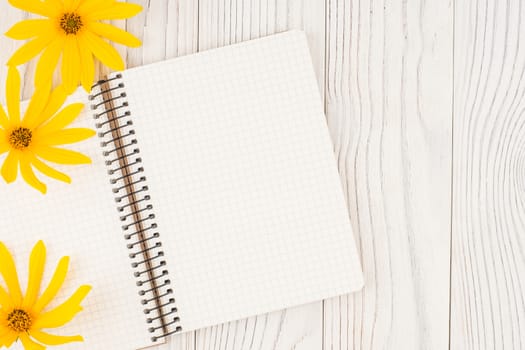 Notebook with yellow wild flowers on  old wooden table. Top view.