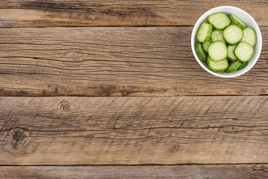 Cut cucumbers in a white bowl on old wooden table. Selective focus.