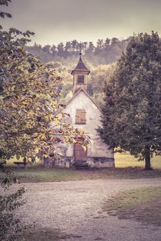 Image in retro style depicting autumn at countryside with walnut tree branches in foreground and aged German church in the background.