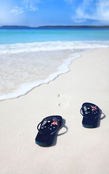 Australian flag thongs on the beach with footprints leading into the ocean.  Holiday, vacation, travel, leisure, unwind