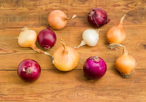 Several onion bulbs different varieties scattered on a surface of the old  darkened by time wooden planks 
