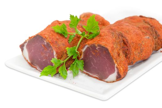 Two pieces of dried pork tenderloin and twig of parsley on a white dish closeup on a light background 
