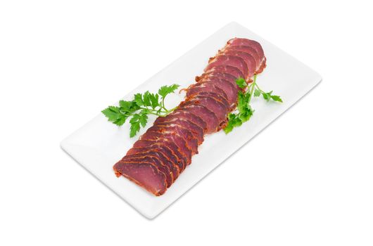 Sliced dried pork tenderloin with twigs of parsley on a white rectangular dish on a light background 
