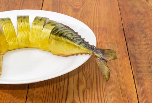 Fragment of a white dish with several slices of a cold-smoked Atlantic mackerel on an old wooden surface
