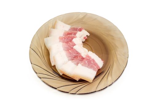 Uncooked sliced pork fatback with a skin and layer of meat on the glass saucer on a light background
