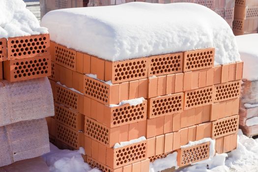 Red perforated bricks with round holes covered snow on a pallet on an outdoor warehouse in winter sunny day

