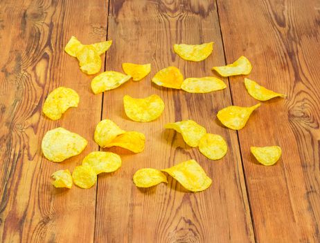 Potato chips scattered on the surface of the old darkened by time wooden planks
