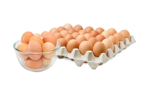 Glass bowl with the brown chicken eggs against the background of the cardboard egg tray of eggs on a light background
