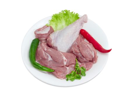 Uncooked turkey meat with the lettuce, parsley and the green and red chili on a white dish on a light background
