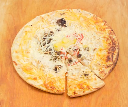 Cooked and partly sliced round pizza with mushrooms, tomatoes and plenty of cheese on a wooden cutting board
