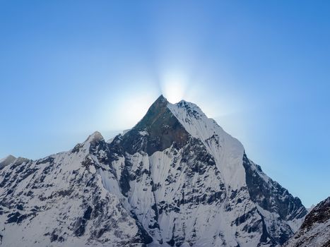 Mountain peak covered glaciers and rays of rising sun from behind him against the background of the sky early morning in the Himalayas
