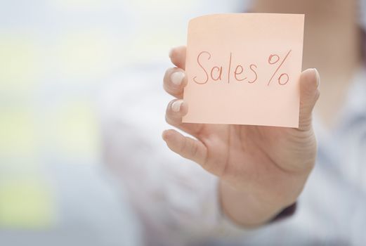 Hands holding sticky note with Sell percent text