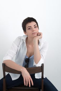 Young beautiful sexy smiling girl in shirt sitting on chair isolated on the white background, looking at the camera.