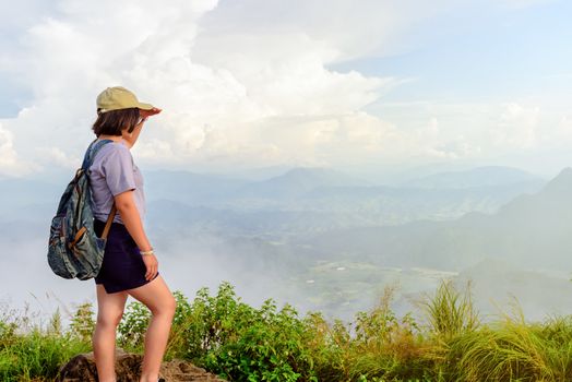 Traveler teens girl hiker wear cap and glasses with backpack looking beautiful nature landscape on high mountain at viewpoint of Phu Chi Fa Forest Park during sunset in Chiang Rai Province Thailand
