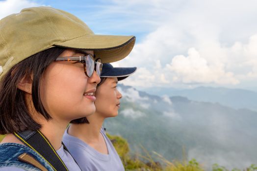 Face two young women hiker, mother and daughter smiling happily while looking beautiful landscape nature of mountain range and sky at Phu Chi Fa Forest Park, Chiang Rai, Thailand