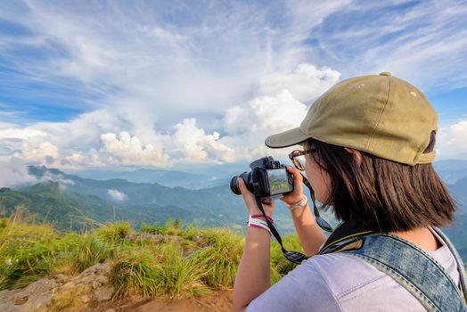 Hiker asian teens girl with backpack looking photo on digital camera is beautiful landscape natural of sierra and sky during sunset on mountain at Phu Chi Fa Forest Park, Chiang Rai, Thailand