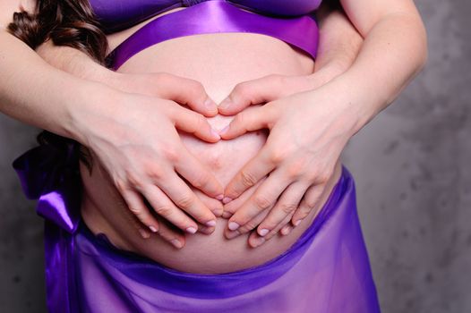 husband hugging his pregnant wife and make heart fingers on her stomach