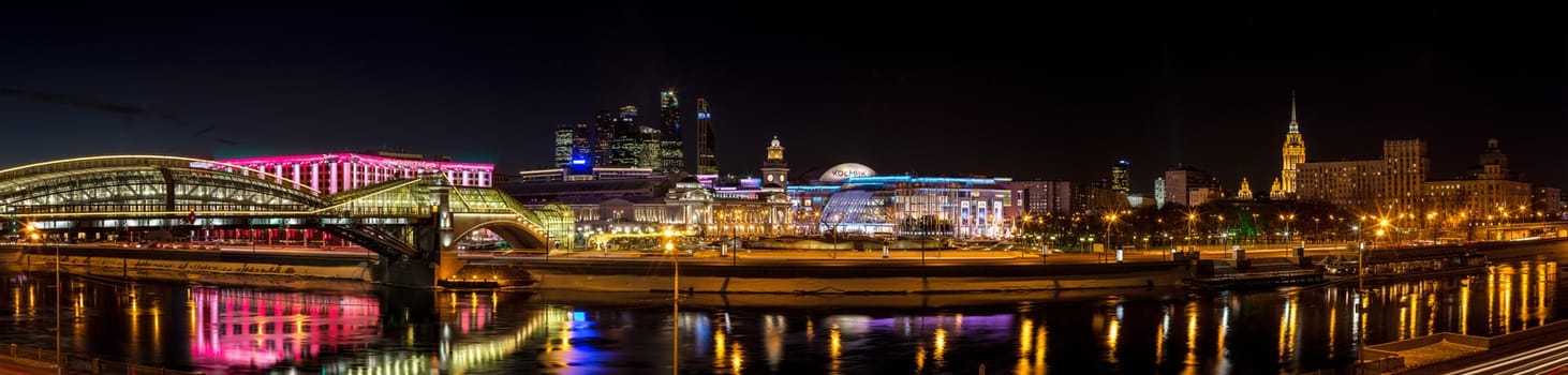 Night winter panorama of the Moskva River embankment: pedestrian bridge Bogdan Khmelnitsky, Kiev railway station, Moscow-City, Redisson Slavyanskaya hotel, "Europe" Square, shopping center "European", Radisson Royal Hotel (the former "Ukraine"). Rich colorful illuminations and reflections in the river.