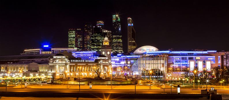 Night winter panorama of the Moskva River embankment: Kiyevskaya railway station, Moscow-City, shopping center "European". Rich colorful illuminations and reflections in the river.