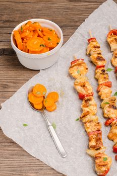Skewers of grilled chicken satay with red peppers and onions with and sauteed carrots
