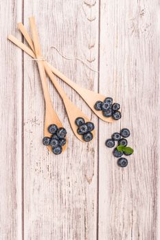 Fresh blueberries with wooden spoon and mint leaf on rustic textured background. Top of view with copy space