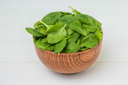 Spring spinach leaves in the bowl. White wooden background