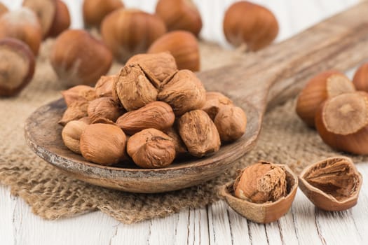 Hazelnut in wooden spoon ins old white wooden table. Selective focus.