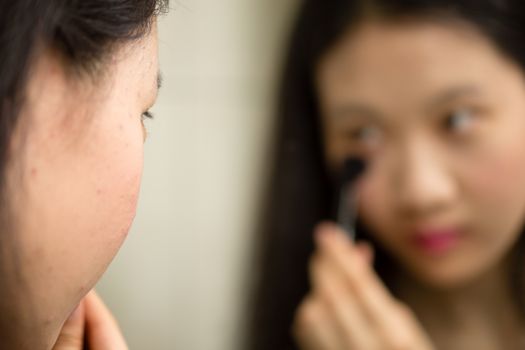 Chinese teenager putting on makeup with brush in front of mirror