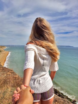 Follow me. Blonde girl standing back on the edge cliff