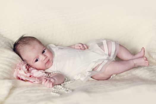 Newborn baby girl in fshionable dress with flower and pearl beads