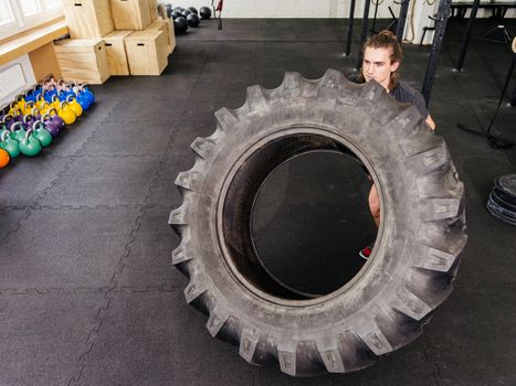 Photo of an attractive young man working out with a tractor tire at a gym.