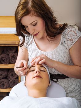 Photo of a beautician plucking the eyebrows of a young woman in a spa.