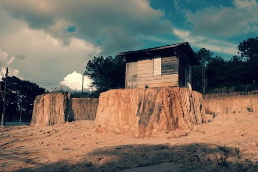 Lonely old wooden house on earth mound after scoop soil for clearance at Da Lat, Viet Nam make funny scene