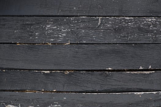 Black peeling, crackled, weathered horizontal wooden barn boards with straw