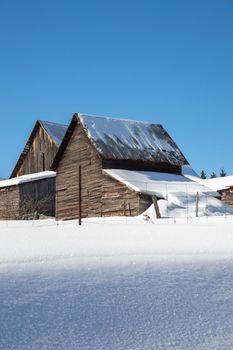 Two snow covered barns in the sunshine in Northern Ontario. Blue sky and fresh white snow. Copy space at the bottom in the snow.