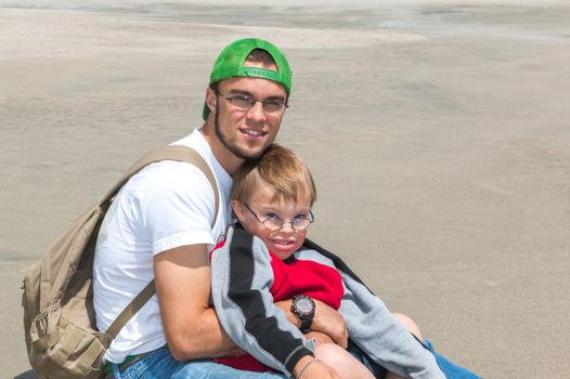 Little Brother With Downs Syndrome Sitting With Big Brother at the Beach