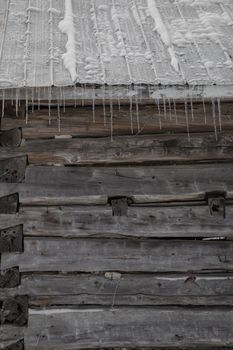 Wintertime snowy old pioneer log cabin barn with icicles. Closeup